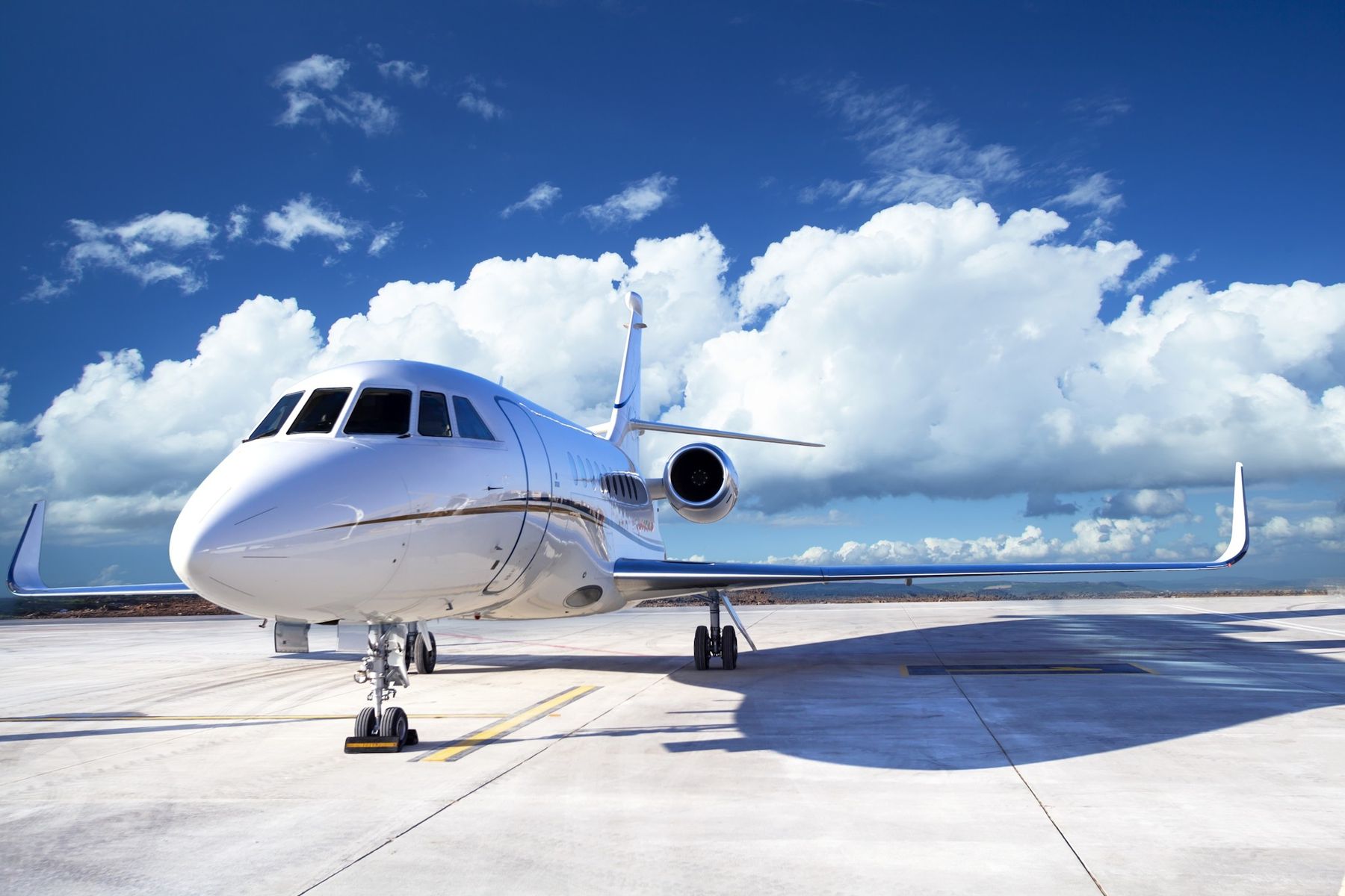 A white business jet parked on a concrete apron under a deep blue sky with large white clouds