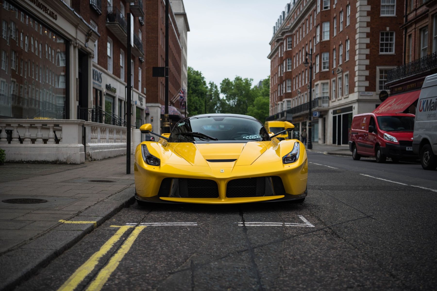 A yellow Ferrari hypercar parked on a London street lined with red-brick mansion blocks