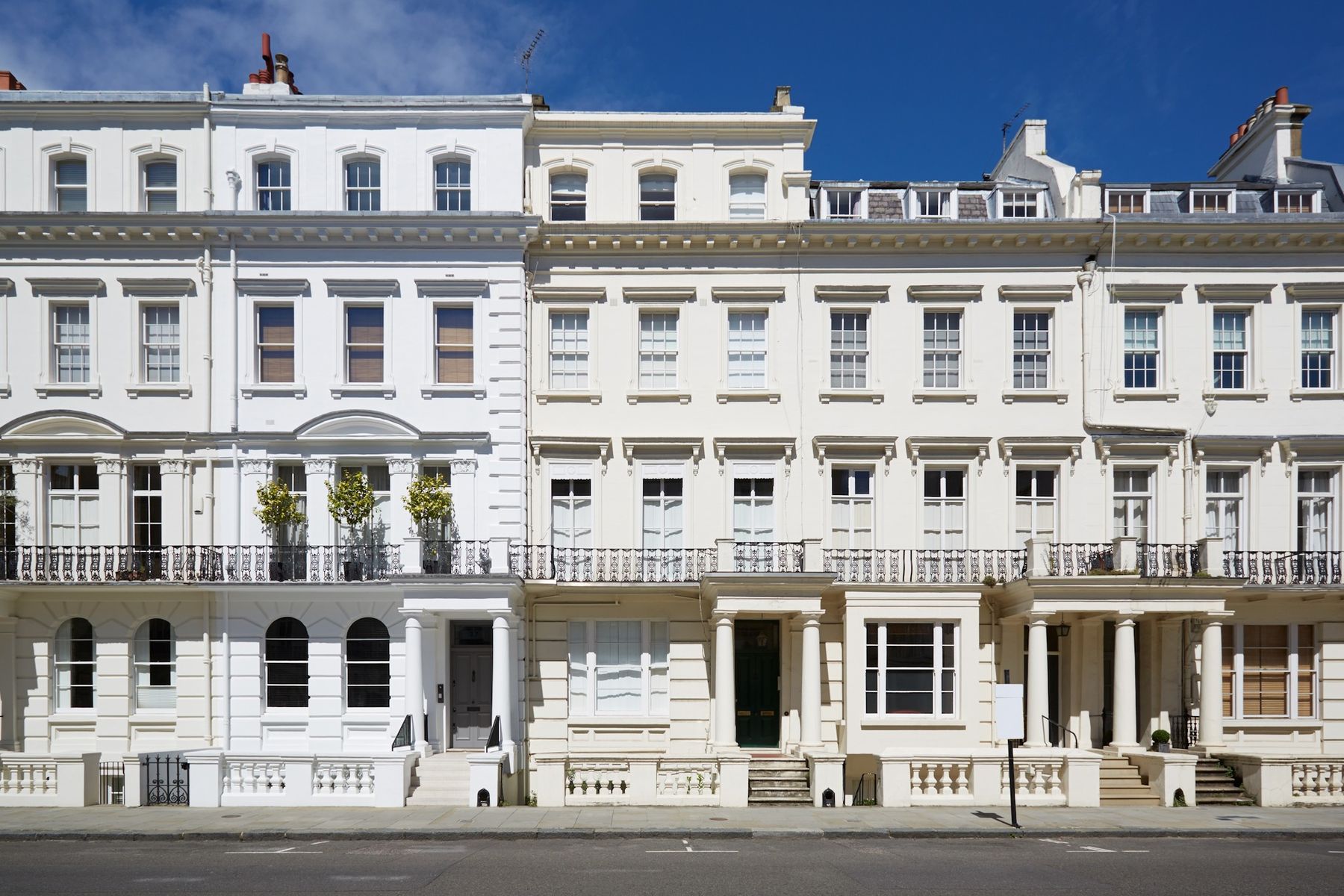 A row of white stucco townhouses with columned porches and black iron balconies under a blue sky
